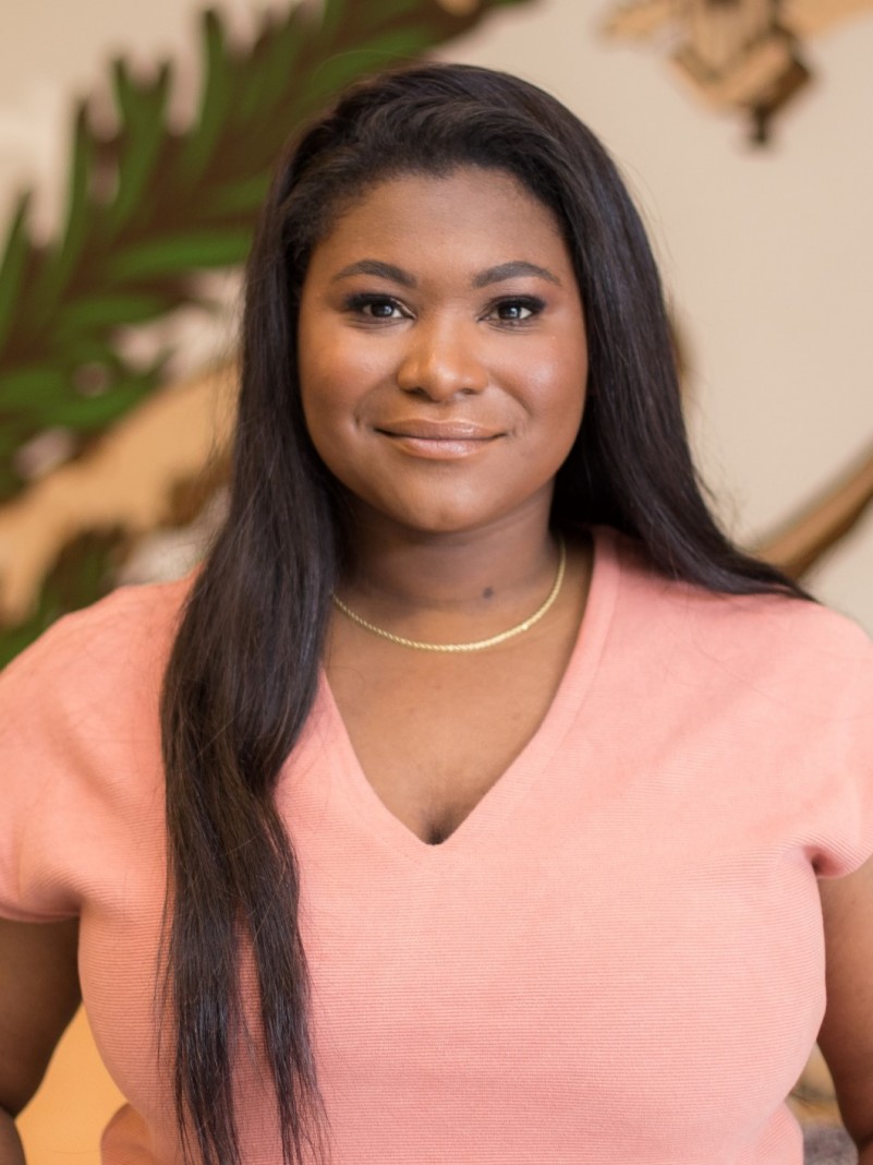 Retrato da secret&aacute;ria de Inclus&atilde;o Digital e Apoio &agrave;s Pol&iacute;ticas para Equidade, Lisiane Lemos. Ela &eacute; uma mulher negra, de cabelo preto liso, vestindo uma blusa de cor salm&atilde;o e um colar dourado.